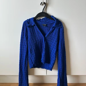 Blå strukturerad kofta från Monki - Säljer en blå kofta från Monki i storlek S. Tröjan har lång ärm, krage och är gjord i ett vågigt, strukturerat material som ger en unik look. Perfekt för dig som vill sticka ut med färg och textur i din outfit.