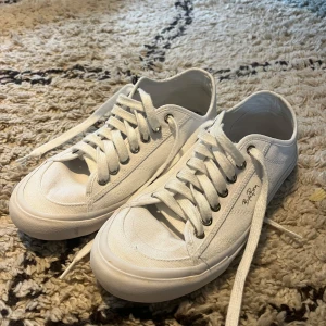 Vita sneakers från Björn Borg - Klassiska vita sneakers från Björn Borg med lågt skaft och rund tå. Skorna har snörning med metallhål och är tillverkade i canvas med vit gummisula. Perfekta för en clean och stilren look.