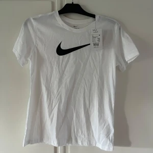Vit Nike t-shirt - Vit t-shirt från Nike med klassisk logga på bröstet och mjukt material. Säljes ny med prislapp då den inte kommit till användning och bara tar plats i garderoben🤍