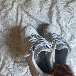 Nike Air Force 1 vita sneakers - Klassiska Nike Air Force 1 i helvitt skinn med lågt skaft och perforerad tå. Snygg och tidlös modell med vit sula och snörning. Perfekta för dig som gillar streetstyle och vill ha en ikonisk sneaker i garderoben men under det finns bara lite skada. Skorn har storlek 40.5 men även passar 41 .