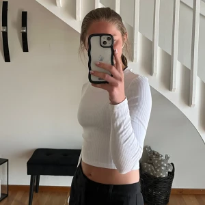 Vit croppad långärmad topp - Säljer en vit croppad långärmad topp med ribbad struktur. Toppen har rund halsringning och sitter tight mot kroppen, perfekt att styla med höga byxor eller kjol. Enkel och stilren design som funkar till det mesta🤩