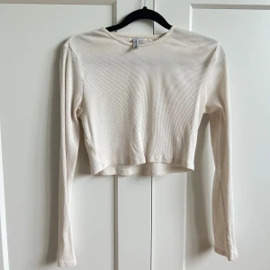 Gräddvit croppad långärmad tröja - Säljer en gräddvit croppad långärmad tröja från H&M Divided. Tröjan är ribbad och har en enkel, stilren design med rund halsringning. 