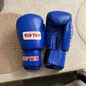 Blå boxningshandskar från Top Ten - Säljer ett par blå boxningshandskar från Top Ten. Handskarna har en klassisk form med bred kardborrestängning och tydlig logga på ovansidan och handleden. Perfekta för dig som vill träna boxning eller kampsport. Handskarna är legitimerade matchandskar  och är iba approved vilket menas att de används i matcher. Extremt bra skick. Använd 2-3 träningar. Original pris runt 1500-2000 men säljer för 1000 för att få bort de snabbt. Pris kan sänkas vid snabb affär.