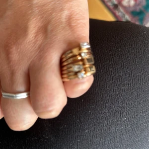 Edblad Guldiga stapelringar st 16  - Säljer ett set med sex tunna guldiga stapelringar, var och en prydd med en liten fyrkantig klar sten. Ringarna har en minimalistisk och modern design som är superenkel att matcha med andra smycken. Perfekt för dig som gillar att mixa och stapla flera ringar på samma finger.