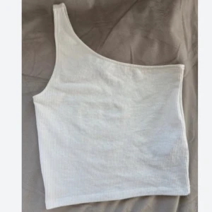 Vit one shoulder topp  - Säljer en vit ribbad one shoulder topp från Gina Tricot i storlek XXS. Toppen är ärmlös och har en tight passform 