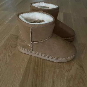 Bruna mockaboots med foder - Mysiga bruna boots i mocka med mjukt vitt foder på insidan. Skorna har rund tå, platt sula och synliga sömmar som ger en chill look. Perfekta för kalla dagar när du vill hålla fötterna varma och sköna.