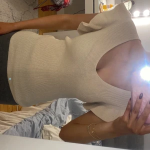 Beige stickad topp med volang - Säljer en beige stickad topp med volangdetalj vid axeln och djup v-ringning. Toppen är figurnära och har korta ärmar. Perfekt för dig som gillar stilrena och trendiga plagg. Strl M men passar också XS/S