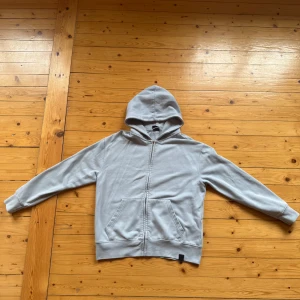 Ljusblå hoodie från Pull&Bear - En stilren ljusblå hoodie från Pull&Bear med dragkedja framtill och två stora fickor. Tröjan har huva och är tillverkad i mjuk bomullsmix, perfekt för chill dagar. Klassisk passform och långärmad design.