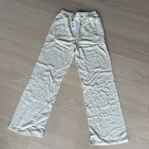 Beiga linnebyxor från Grunt XL - Snygga och luftiga linnebyxor från Grunt i en ljus beige färg. Byxorna har rak passform, resår i midjan med snörning och är perfekta för varma dagar. Materialet är 100% linne och färgen kallas sand.