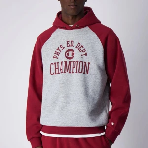 Champion hoodie röd/grå med tryck M - Helt ny skick. Nypris 800kr. Snygg hoodie från Champion i rött och ljusgrått med klassiskt tryck på bröstet. Tröjan har huva, raglanärmar och ribbade muddar. Perfekt för chill dagar eller när du vill ha en sportig vibe. Materialet är mjuk bomullsmix.