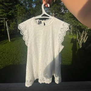 Vit spetsblus från Pieces - Superfin vit blus från Pieces med vackra spetsdetaljer och broderat mönster. Blusen har korta ärmar med bred spetskant och rund halsringning med knapp i nacken. Perfekt för en somrig look med romantiska vibes. Frakten kan diskuteras💗