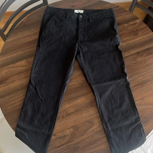 Svarta chinos från Pier One, stl 33 - Svarta chinos från Pier One i storlek 33. Klassisk rak passform med bälteshällor, knapp och dragkedja framtill samt diskreta bakfickor. Tillverkade i mjuk bomullsmix som känns skön mot huden. Perfekta för en clean och stilren look.