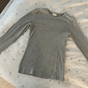 Grå ribbad långärmad tröja - En enkel och stilren grå långärmad tröja från Gina Tricot. Tröjan är ribbad och har en rund halsringning. Perfekt att styla med jeans eller kjol för en clean look. Materialet är mjukt och stretchigt, vilket gör den riktigt skön att bära.