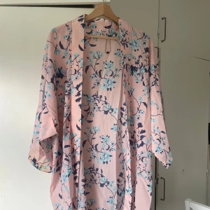 Blommig cardigan - Säljer en superfin overshirt i ljusrosa med blått blommönster. Jackan har lös passform, trekvartsärmar och är tillverkad i ett lätt polyestertyg. Perfekt att slänga över en t-shirt för en chill och trendig look.