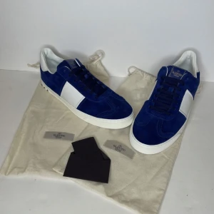 Blåa Valentino sneakers i mocka - Snygga blåa sneakers från Valentino med vit detalj på sidan och vit sula. Skorna är gjorda i mjuk mocka och har klassisk snörning. Perfekta för dig som vill sticka ut med stilrena och exklusiva sneakers.
