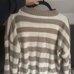 Randig stickad tröja i beige och vitt - Supermysig stickad tröja med breda beige och vita ränder. Tröjan har en relaxed fit, ribbad rund halsringning och långa ärmar. Perfekt för lager-på-lager och chill dagar.