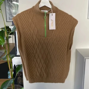 Stickad Väst från Only!  - Säljer en snygg beige stickad väst från ONLY i storlek M. Västen har ett coolt mönster och en grön dragkedja framtill. Perfekt för höst, vår och vinter,  den är i nytt skick. Passar bra till både vardag och fest!