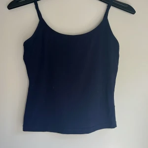 Mörkblå linnetopp med smala axelband - Enkel och stilren mörkblå linnetopp med smala axelband och rak passform. Perfekt att matcha med jeans eller kjol för en clean look. Mjuk och skön bomullskänsla, passar dig som gillar minimalistisk stil.