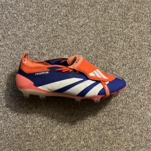 Adidas Predator fotbollsskor blå/orange Elit - Säljer ett par Adidas Predator fotbollsskor i blått, orange och vitt. Skorna har snörning, täckt plös och tydliga Predator-detaljer. Ovandelen är i syntetmaterial med Hybridtouch 2.0 och dobbar för gräsplan. Perfekta för dig som vill sticka ut på planen. Använt ett par träningar och matcher. Ny pris 3000.