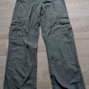 Olivgröna cargopants med stora fickor - Säljer ett par olivgröna cargopants med bred passform och stora fickor på sidorna. Perfekta för en avslappnad och cool stil. Har extremt fin passform säljer för att det är inte min stil längre. Använd fåtal gånger.
