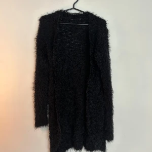 Svart fluffig kofta i lång modell - Mysig svart kofta med fluffig textur och lång passform. 