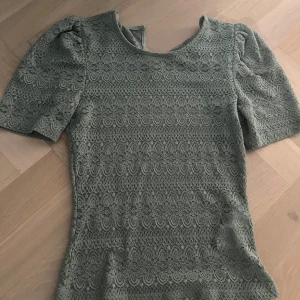Grön spetsblus från VILA  - Supersöt grön blus från VILA i storlek XS. Blusen har korta ärmar och är helt täckt av ett detaljerat spetsmönster som ger en romantisk vibe. Perfekt när du vill sticka ut lite extra med en unik topp!