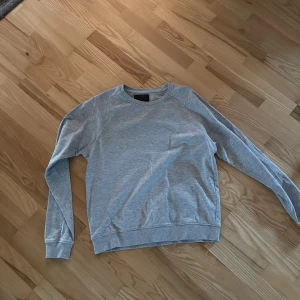 Ljusgrå basic sweatshirt - En stilren ljusgrå sweatshirt med rund hals och långa ärmar. Tröjan har en klassisk passform och är tillverkad i mjuk bomullsmix, perfekt för en avslappnad look. Ribbstickade muddar vid ärmslut och nederkant ger en snygg finish.