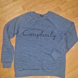 Blå sweatshirt från Amisu med text - Blå sweatshirt från Amisu i storlek XS med broderat blommönster och texten 'Completely in love' framtill. Tröjan har rund hals, långa ärmar och ribbade muddar. Perfekt för dig som gillar unika detaljer och en chill stil.