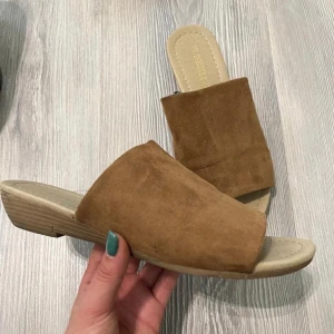 Bruna mockasandaler med låg klack - Snygga bruna sandaler i mocka med öppen tå och låg klack. Perfekta för varma dagar och ger en chill vibe till din outfit. Bred rem över foten och platt sula för extra komfort.