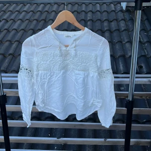 Vit blus med spetsdetaljer KappAhl - Supersöt vit blus från KappAhl med broderade spetsdetaljer och långärmade ärmar. Blusen har en avslappnad passform, rund halsringning och fina virkade partier på ärmar och bröst. Tillverkad i viskos och polyester för en lätt och luftig känsla.