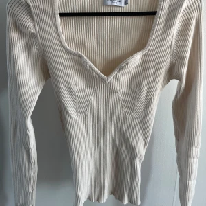 Ribbad beige långärmad tröja  - Supersnygg ribbad beige tröja med v-ringad hals och lång ärm. Tröjan har en figurnära passform och är tillverkad i ett stretchigt material som sitter riktigt bra. Perfekt att styla med jeans eller kjol för en clean look.