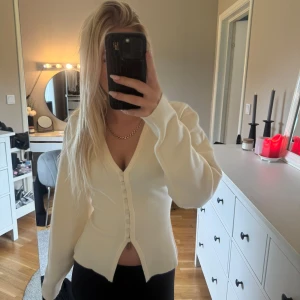 Vit kofta med knappar från Gina Tricot - Supersnygg vit kofta från Gina Tricot i stickat material. Modellen har v-ringning, figurnära passform och knappar framtill. Perfekt att styla med jeans eller kjol för en clean och fräsch look.