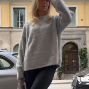 Grå oversized stickad tröja - Mysig grå stickad tröja med oversized passform och långa ärmar. Tröjan har en enkel design och är perfekt för lager-på-lager-stil. Den är fluffig och har en avslappnad vibe, perfekt att slänga på sig när det är kyligt ute.