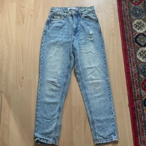 Mom jeans från FB Sister, ljusblå XS - Ljusblå mom jeans från FB Sister i klassisk denim med hög midja och raka ben. Jeansen har slitna detaljer framtill och femficksmodell. Perfekt för dig som gillar en avslappnad och trendig look.