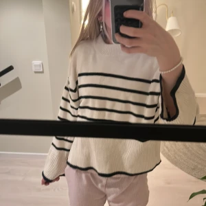 Vit och svart randig tröja från Gina Tricot - Säljer en snygg vit tröja med svarta ränder från Gina Tricot. Tröjan har långa ärmar och en ribbad kant vid halsen, ärmsluten och nederkanten. Perfekt för en stilren look!