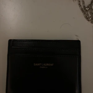 Svart plånbok från Saint Laurent - Snygg och stilren svart plånbok från Saint Laurent i skinn. Perfekt för att hålla dina kort och kontanter organiserade. Den har flera kortfack och en elegant design med Saint Laurent-logotypen i guld på framsidan.