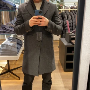 Sand Copenhagen kappa 46/S - Säljer en elegant grå kappa i en lyxig blandning av ull och kashmir. Köpt på NK för 5000kr år 2023, säljer nu för 2299. Fint skick, kommer med avtagbar väst och 2 extra knappar! STORLEK 46/S