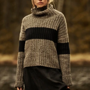 Grå och svart stickad polotröja från Nygårdsanna - Säljer en snygg grå och svart stickad polotröja från Nygårdsanna. Tröjan har en bred svart rand över bröstet och ärmarna, samt en hög polokrage. Perfekt för kyliga dagar med sin mysiga och varma design samt tumhål.  Lånad produktbild för passform. Har lite noppor som ulltröjor lätt får men inga andra anmärkningar.  Storlek M, rymlig modell. Hund finns i hemmet.