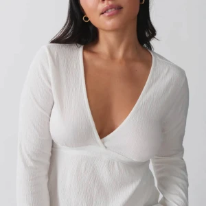 Vit blus/top - Snygg vit blus/ top från gina med v-ringning och långa ärmar. Toppen har en knytning i ryggen som ger en fin passform. 