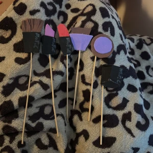 Handgjorda sminkverktyg i foam papper - Unika handgjorda sminkverktyg i mjukt foam papper, inklusive sminkborste, läppstift, nagellack och ögonskugga osv. Perfekt för lek och kreativitet. Verktygen är färgglada och detaljerade, med en mix av lila, rosa, rött, grönt, svart och brunt.