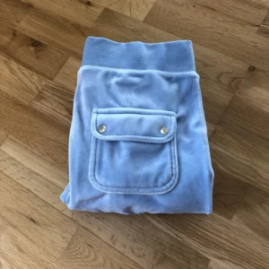 Turkos/ ljus blå mjukisbyxa med fickdetalj - Säljer ett par Juicy Coutoure mjukisbyxor med en snygg ficka bak som har knapplås. Byxorna har en bekväm resår i midjan. Str L men sitter som en s/m