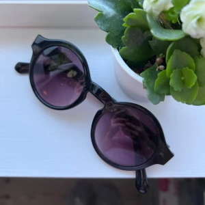 Svarta runda solglasögon - Snygga svarta solglasögon med rund form och mörka linser. Perfekta för en stilren look. Bågarna är robusta och ger en klassisk känsla. Passar bra till både vardag och speciella tillfällen 💜 Önskar du exakta mått? Tveka inte att höra av dig!