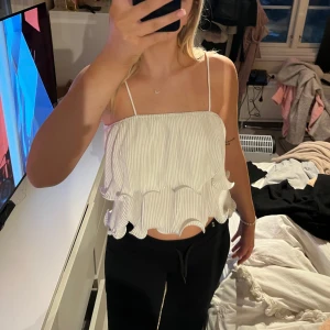 Vit ärmlös topp med volanger - Säljer en söt vit ärmlös topp med tunna axelband och volanger. Perfekt för sommardagar eller en avslappnad kväll. Toppen har en luftig och lätt design som ger en romantisk känsla.