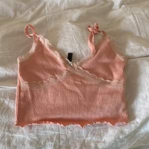 Söt rosa ribbad linnetopp från H&M Divided med spetsdetaljer och justerbara axelband. Perfekt för varma dagar eller som ett lager under en tröja. Den har en omlott-design framtill som ger en fin passform.