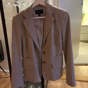 Beige/grå kavaj från Banana Republic - Elegant beige/grå kavaj från Banana Republic med klassisk design och två knappar framtill. Perfekt för en stilren look. Tillverkad i ett mjukt material som ger en bekväm passform. Skulle säga att den passar xs-s