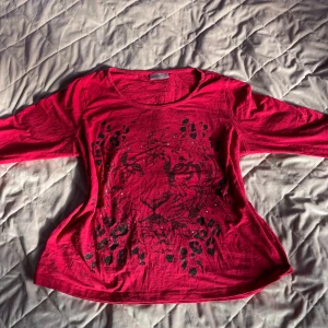Röd trendig topp med leopardmönster - Säljer en röd trendig topp från Isolde med ett coolt leopardmönster i svart. Toppen har trekvartsärmar och en rund halsringning. Perfekt för att ge din outfit en edgy touch! Storlek L! Öppen för prisförslag 