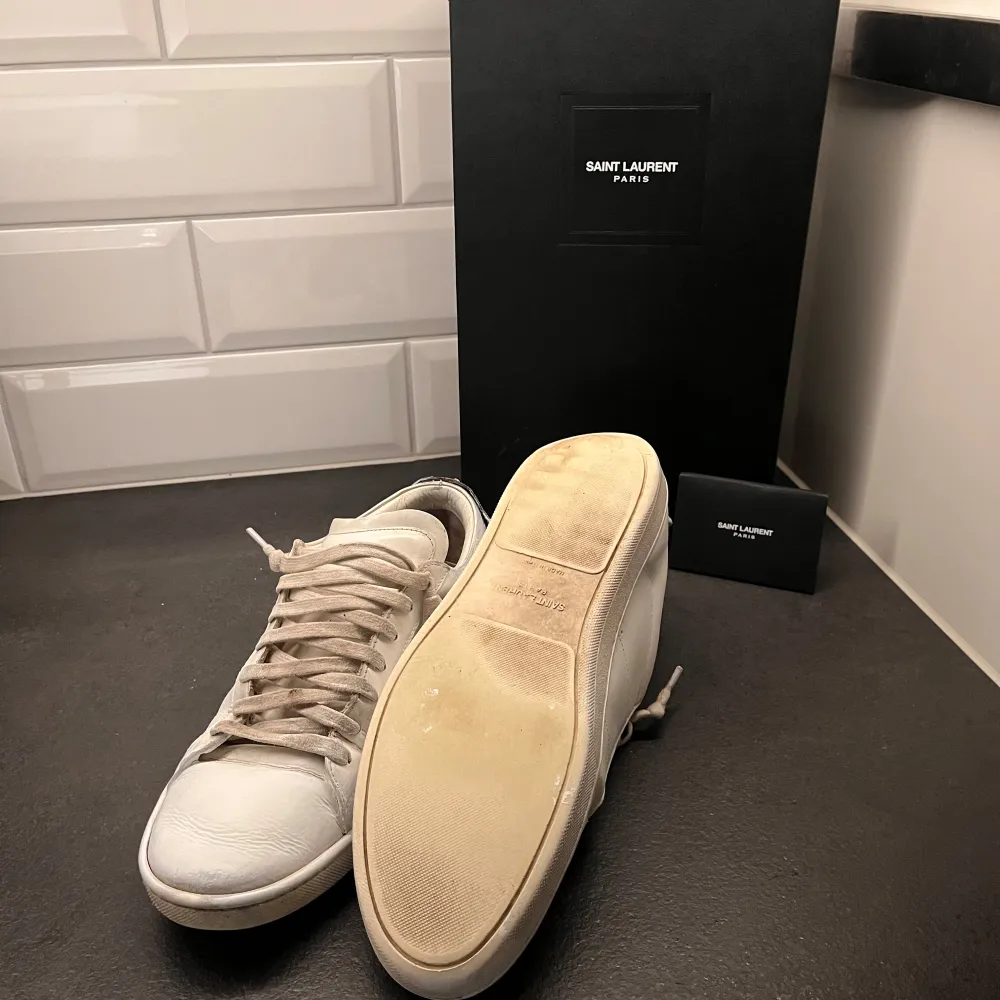 Snygga vita sneakers från Saint Laurent med unika läppdetaljer i rött och blått på hälen. Model sl/01, perfekta inför sommaren. Finns en del skavanker och dem är rätt så välanvända. Box, påse och certifikat med följer, inne sulan är dock inte orginal. Hör av er vid minska fråga✌️. Kengät.