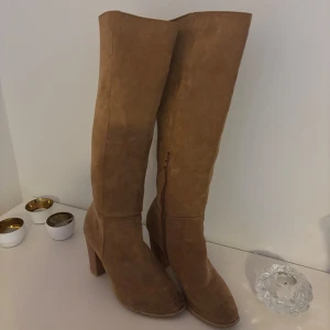 Bruna mockastövlar med klack - Snygga bruna stövlar i mocka med hög klack och dragkedja på sidan. Perfekta för höst och vinter, dessa stövlar ger en elegant touch till din outfit.