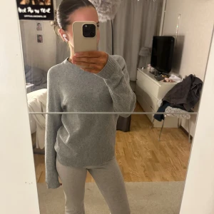 Grå stickad tröja - Säljer en mysig grå stickad tröja med långa ärmar. Perfekt för kyligare dagar och passar till många olika outfits. Tröjan har en enkel och stilren design med ribbstickade muddar vid ärmslut och nederkant.