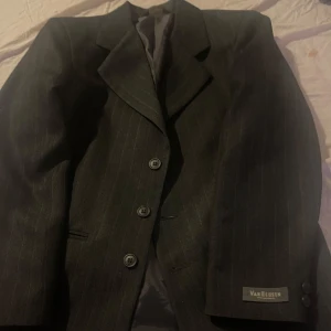 Mörkgrå randig kostym från Van Heusen - Snygg mörkgrå kostym från Van Heusen med diskreta ränder. Kavajen har klassisk design med tre knappar och byxorna har en stilren passform. Perfekt för formella tillfällen. Byxorna är i storlek XS och kavajen är i storlek S. Säljer för att de inte kommer till användning längre. 